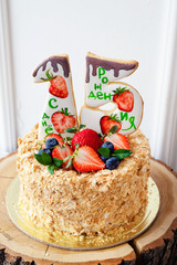 Honey cake decorated with bright strawberries and blueberries with number 15. Festive party cakes for birthday, inscription in Russian.