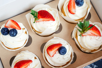 Cupcakes with whipped cream and strawberries and blueberries. Festive party cakes for birthday, wedding.