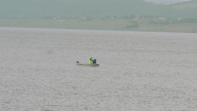  Two fishermen in small boat on a Lake of fjord, bright yellow coat. Closer shot.