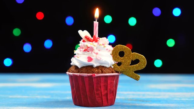 Delicious birthday cupcake with burning candle and number 92 on multicolored blurred lights background