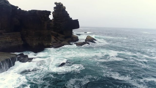 Aerial view stormy waves breaking against rocky coast of Atlantic ocean. Drone flying above water along the coast with steep cliffs and cracked stones in foggy morning. Peniche. Portugal