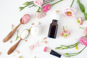 Obraz na płótnie Canvas Set of spa supplies and flowers Overhead bunch of delicate pink flowers placed near bottle of essential oil and smooth cream with salt against white background
