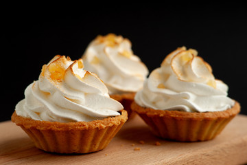 Three cream cakes on a black background. Close-up. Dessert in the form of cakes with protein cream. Cakes look like baskets. Dessert on a black background.