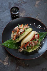 Black plate with a pair of steamed chinese baozi with chicken and vegetables, vertical shot over brown stone surface