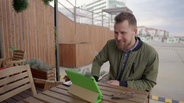Young man is communicating by internet call through tablet sitting outdoors