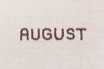The word August written with coffee beans shot from above, aligned in the center, closeup.