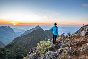 Obraz premium Man stand back to clear sky Cloud wait for sunset at top of wildlife sanctuary name Doi Luang Chiang Dao, Thailand with Shadow of mountain layer and sun ray.