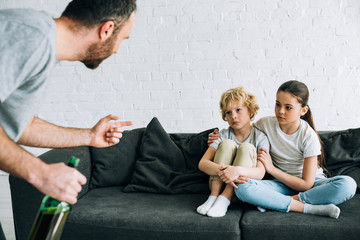cropped view of alcohol addicted father with beer and upset children on sofa