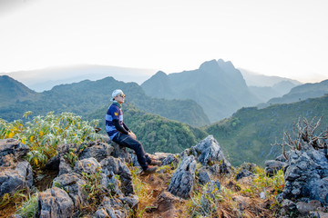 Man sitting back to clear sky Cloud wait for sunset at top of wildlife sanctuary name Doi Luang Chiang Dao, Thailand with Shadow of mountain layer and sun ray.