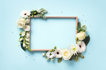 Floral frame of white flowers, green leaves on blue paper background. Flat lay, top view. Spring and summer concept