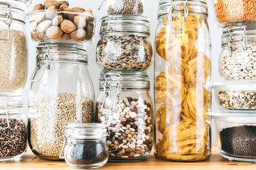 Assortment of uncooked grains, cereals and pasta in glass jars on wooden table. Healthy cooking, clean eating, zero waste concept. Balanced dieting food