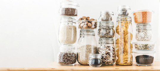 Banner with assortment of uncooked grains, cereals and pasta in glass jars on wooden table. Healthy...