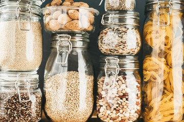 Assortment of grain products and pasta in glass storage containers on wooden table. Healthy...