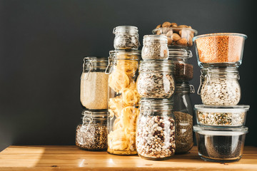 Banner with assortment of grain products and pasta in glass storage containers on wooden table....
