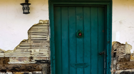 Detail of the frontage of an old abandoned cottage. With weathered door, furniture, exposed original oak beams and lath & plaster rendered construction. England.
