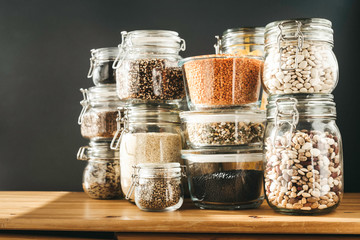Assortment of grain products and pasta in glass storage containers on wooden table. Healthy...