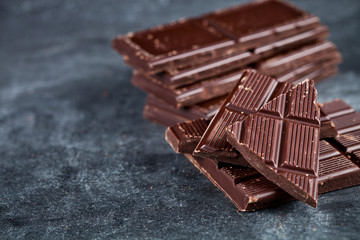  Chunks of broken chocolate stacked on grey background.