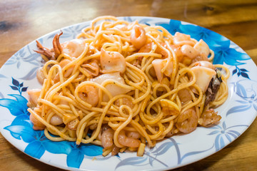 Boiled spaghetti with fried seafood on plate with ornament