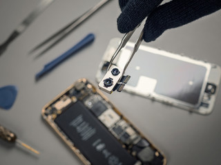 Technician or engineer showing broken dual smartphone camera on blurred smartphone components background