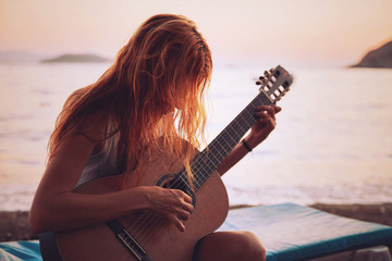 Silhouette of a blonde female playing acoustic guitar on the beach at sunset