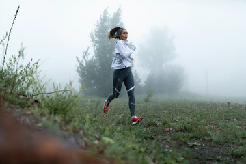 Naklejka na ściany i meble Beautiful female athlete running in nature during foggy morning.