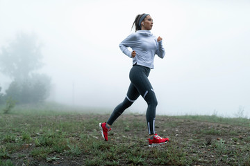Full length of athletic woman jogging in misty day an the park.