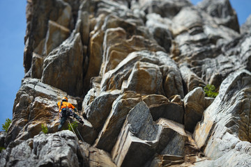Climber climbs up the rock tower against the backdrop of overhanging rocks. Tilt-Shift effect.