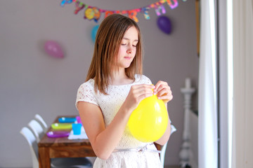 Happy preteen girl blowing yellow balloon decorating house preparing to kids birthday party with set up table and Happy birthday string at background.
