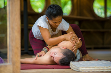 young beautiful and exotic Asian Indonesian therapist woman giving traditional Thai massage to man relaxed at tropical wellness spa in healthy natural lifestyle