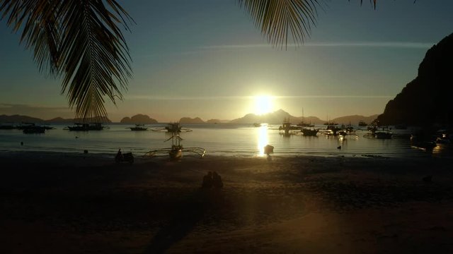 sunset over the beach view through palm tree leaves. Sunset over the sea with islands and boats, Corong corong beach, Palawan, Philippines