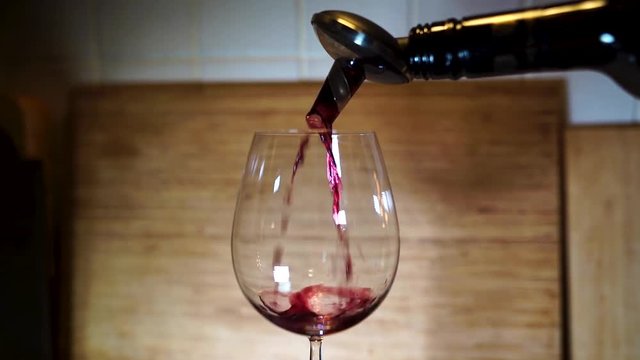 Pouring red vine to vine class with wooden board in the background, shallow depth of view and slow motion