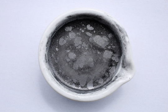 Small particles of aluminum powder are in a ceramic mortar on the surface of the water.