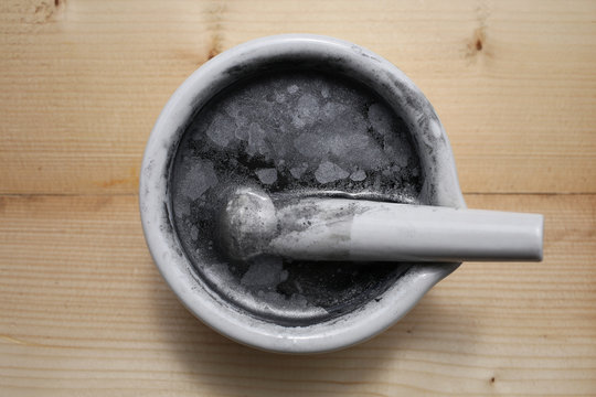 Small particles of metallic aluminum on the surface of the water in a ceramic mortar with pestle.