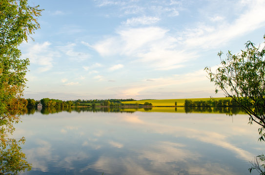 Wild nature, yellow field and sky with reflection in the lake