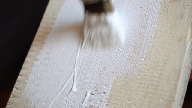 painting a wooden board with a white paint brush close-up