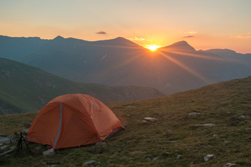 Zoom view of orange tent at sunrise with mountain background and sun
