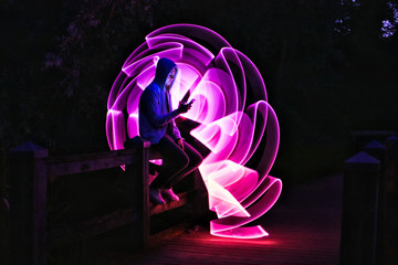Boy sitting on a bridge with his smartphone in his hand. Violet light effect with a light saber in...