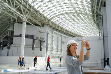 Young girl in a helmet takes pictures on the phone, in the background the workers, an excursion to the construction site, an engineer is satisfied