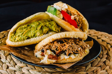 Venezuelan arepas on a black background, made with maize and filled with avocado, tomato, meat, cheese and black beans