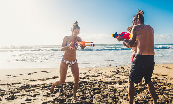 Group of happy young people enjoying the summer holiday vacation at the beach playing with water guns together in friendship having fun - outdoor funny play couples