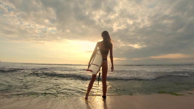 Surfer woman stands with her surfboard on the beach