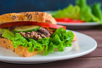 tuna sandwich with tomato cucumber lettuce grilled bread with sunflower seeds on plate soft focus