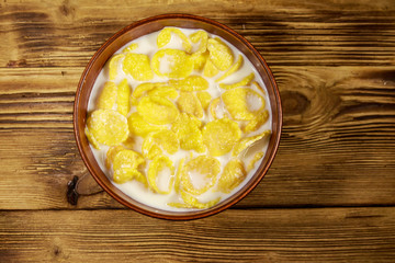 Cornflakes with milk in a bowl on wooden table. Top view