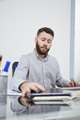 Fototapeta premium Bearded office manager sitting at office desk touching display of tablet pc and reading online message