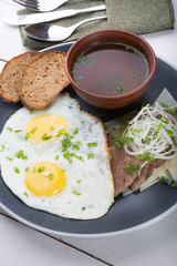 Fried eggs served with bread slices, meat slices and broth
