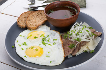 Fried eggs served with bread slices, meat slices and broth