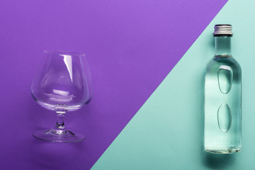 transparent wineglass and bottle with water on bright purple and azure background  