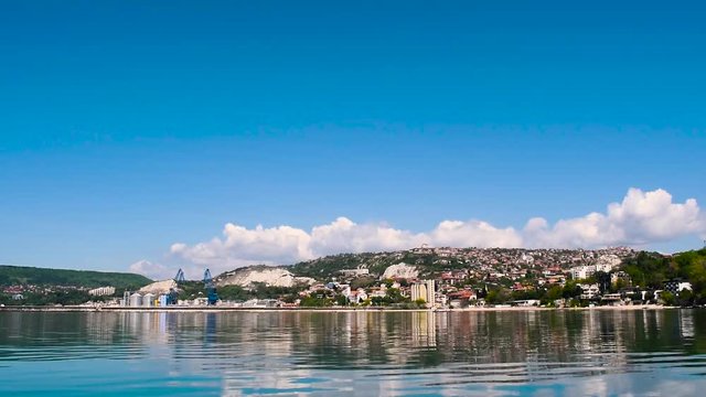 City landscape view from the shore with calm ripples in the water. The city of Balchik on the Black sea. Beautiful fluffy clouds and blue sky in the background. HD 15 seconds footage.