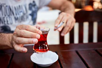 Hands of a caucasian male holding a glass of turkish tea and cigarette at an outdoor cafe