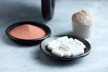 Beta-alanine capsules, Scoop of Whey Protein, Creatine Powder and a dumbbell in background. Sport nutrition. Stone / Wooden background. Copy space